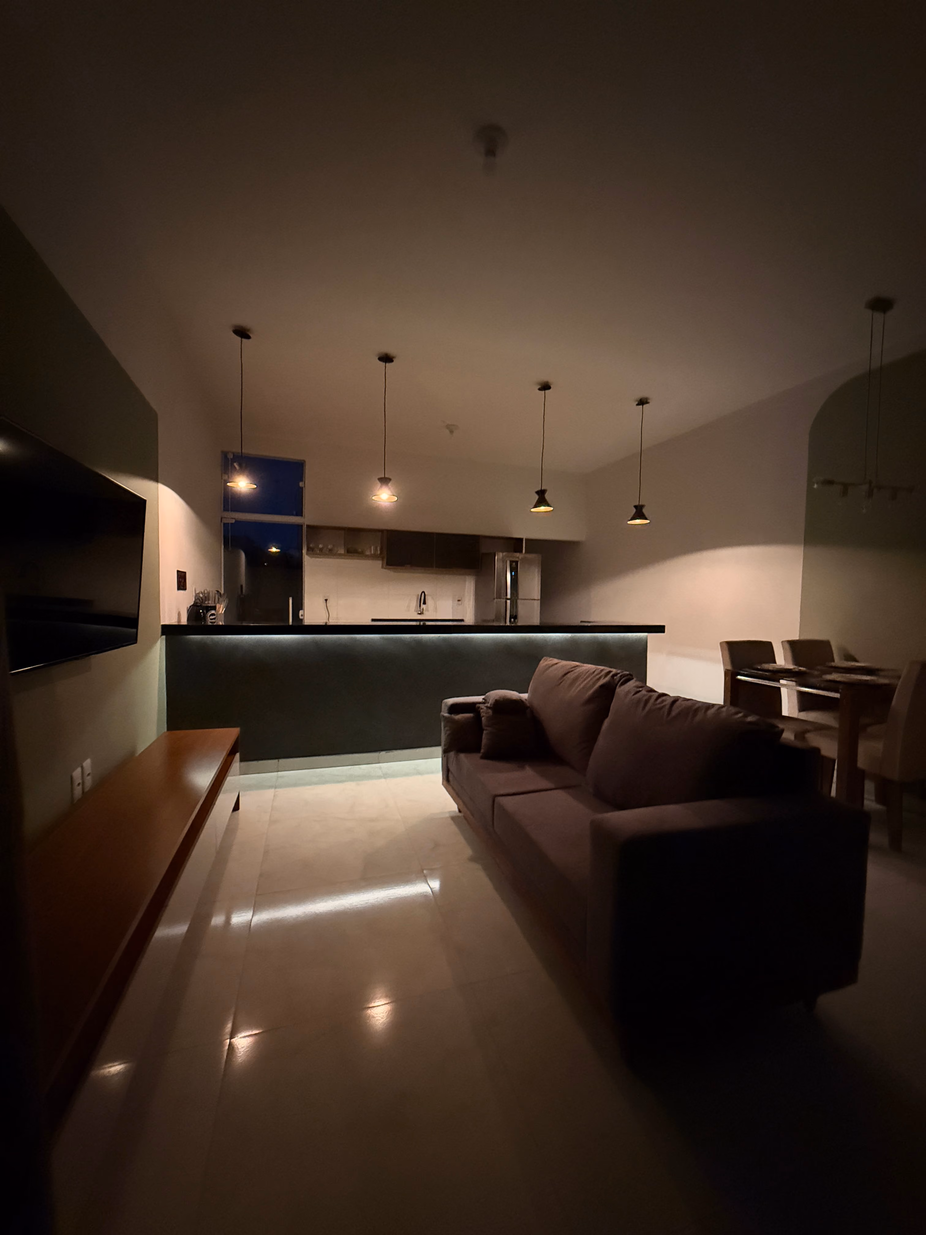 Sala integrada à cozinha da CasaNova à noite, com luz quente acesa